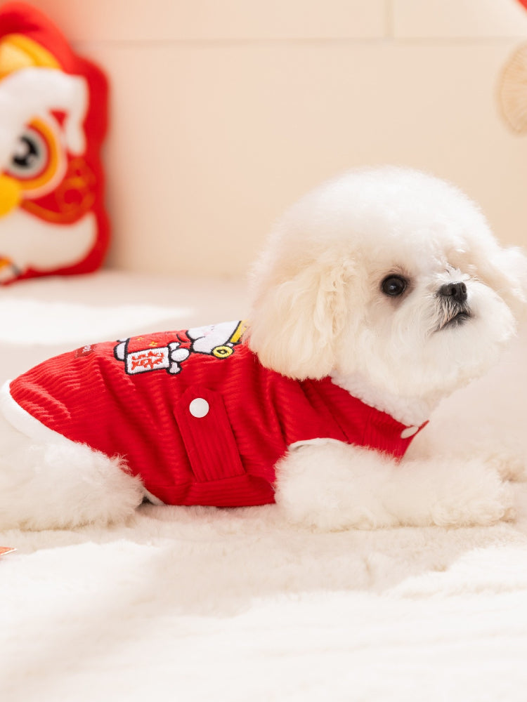 A white dog wearing a red corduroy vest with white button closures and faux fur trim, lying down on a white surface.