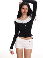 Model wearing a black off-the-shoulder long-sleeved top with white ruffled trim and white shorts.
