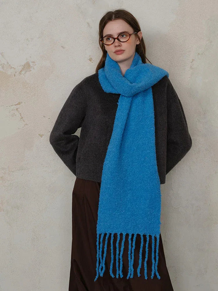 Woman wearing a dark grey sweater and a bright blue textured knit scarf with fringe.