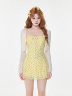 Woman wearing a yellow floral print mini dress with a white sheer cardigan, front view