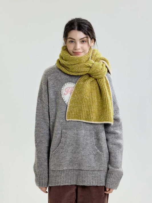 Full-body shot of a model wearing a lime green chunky knit scarf over a grey sweater and brown corduroy pants.