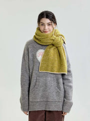 Full-body shot of a model wearing a lime green chunky knit scarf over a grey sweater and brown corduroy pants.