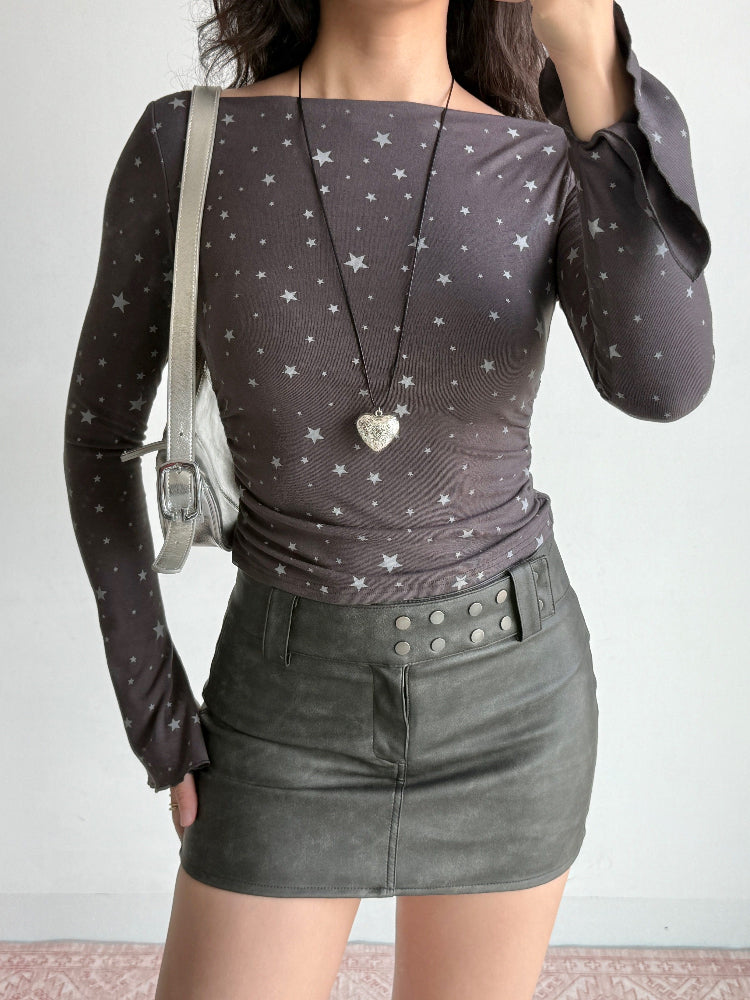 Full body shot of a model wearing a grey long-sleeve top with a white star print, a heart-shaped locket, and a grey leather skirt.