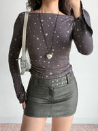 Full body shot of a model wearing a grey long-sleeve top with a white star print, a heart-shaped locket, and a grey leather skirt.