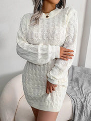 Woman wearing a white cable knit mini dress with long sleeves and a mock neck, with her arms crossed.
