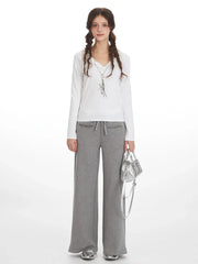 Woman wearing a white long-sleeve shirt and grey wide-leg sweatpants, holding a silver handbag.