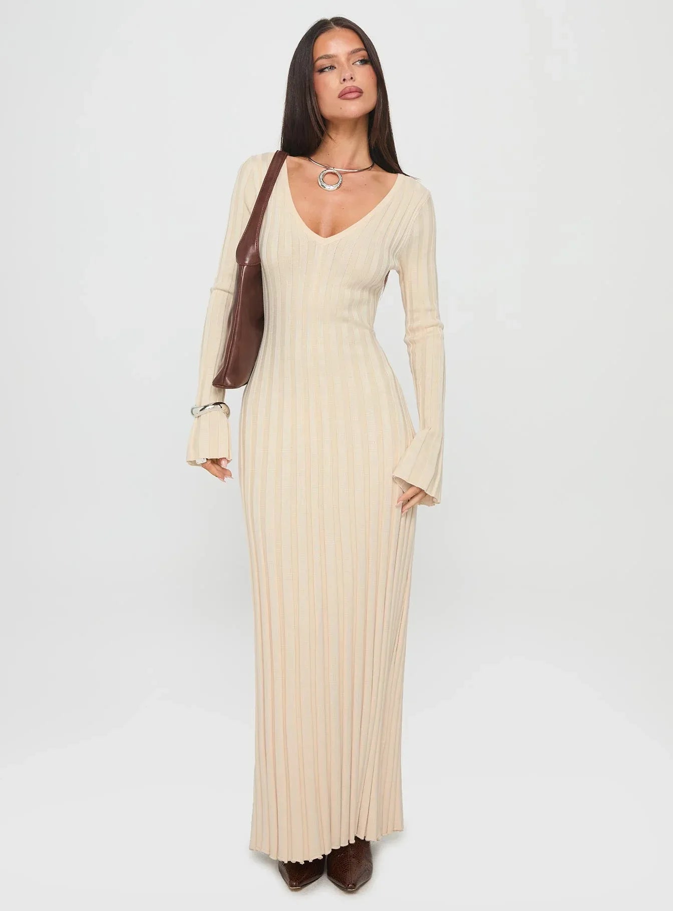 Front view of a woman modeling a cream ribbed knit maxi dress with flared cuffs and a tie waist.
