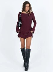 Full length shot of a woman in a burgundy long sleeve mini dress and knee-high black boots