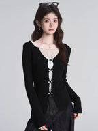 Close-up of a woman wearing a black long-sleeved top with white lace trim and decorative buttons.
