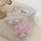 Pink and white iridescent snowflake hair clips on a grey pouch