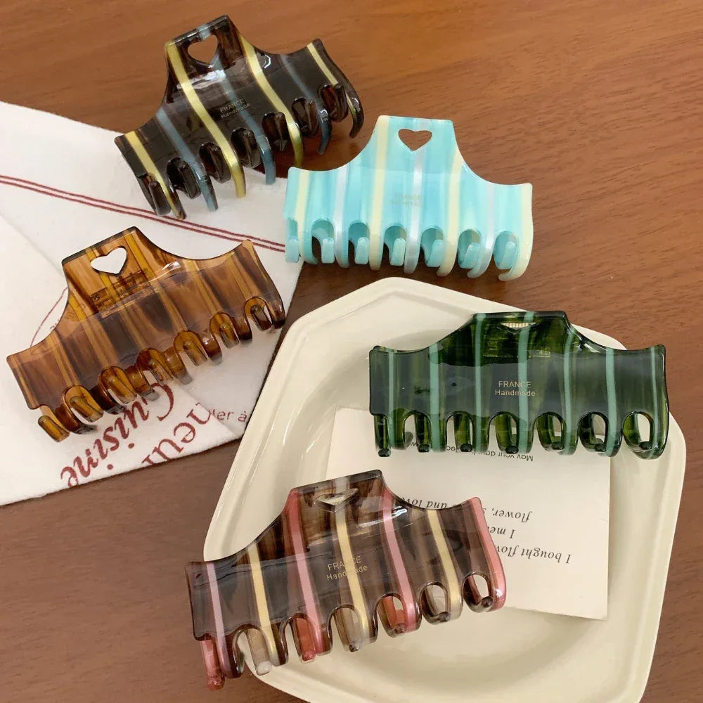 Assortment of striped hair claw clips in different colors arranged on a white plate and fabric