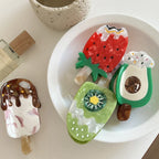 A collection of novelty hair clips, including an ice cream bar, strawberry, avocado, and kiwi slice, arranged on a white surface.