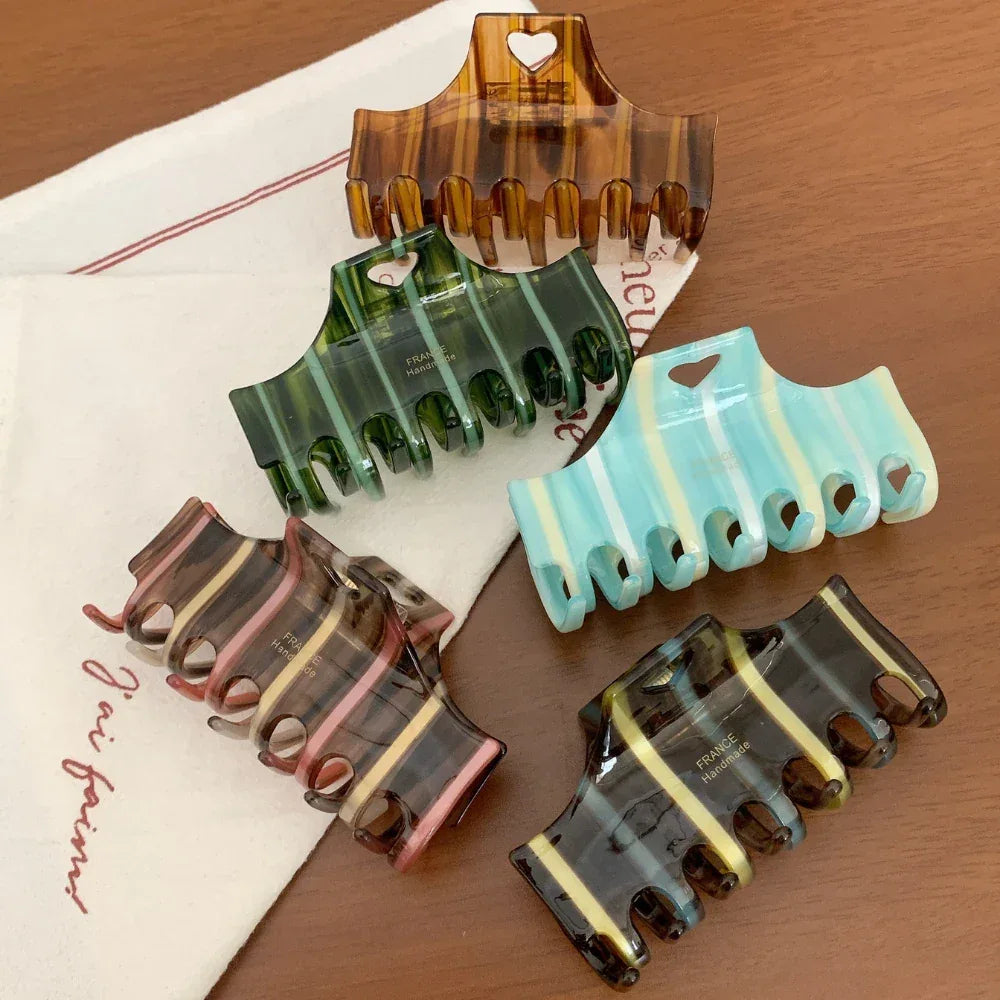 Group of five striped hair claw clips, including brown, green, blue, and pink variations, on a wooden surface
