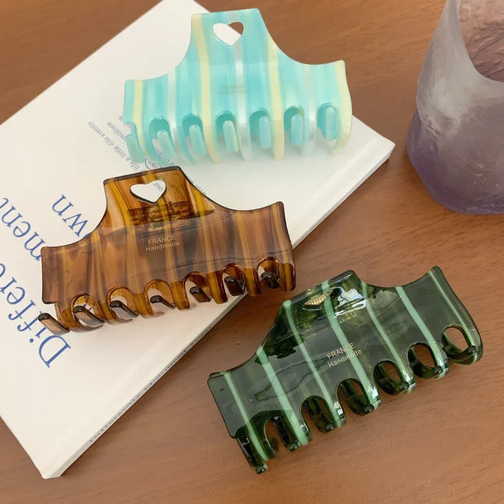Three striped hair claw clips in blue, brown, and green colors placed on a book and next to a glass object