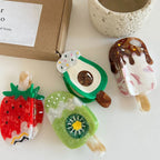 Assortment of fruit and ice cream themed hair clips on a white table, with a box and pot in the background.