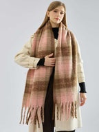 Woman wearing a cream coat and a large plaid scarf, with her hand placed on the scarf.