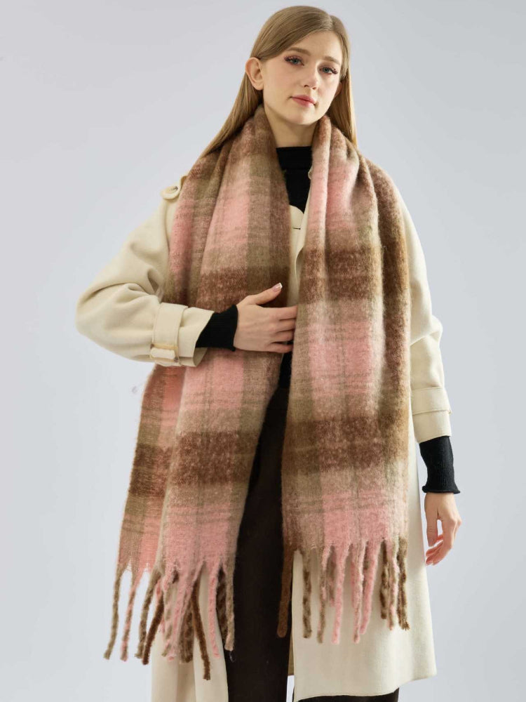Woman wearing a cream coat and a large plaid scarf, with her hand placed on the scarf.
