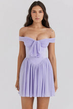 Woman wearing a lavender off-the-shoulder mini dress with a draped bodice and pleated skirt, front view.