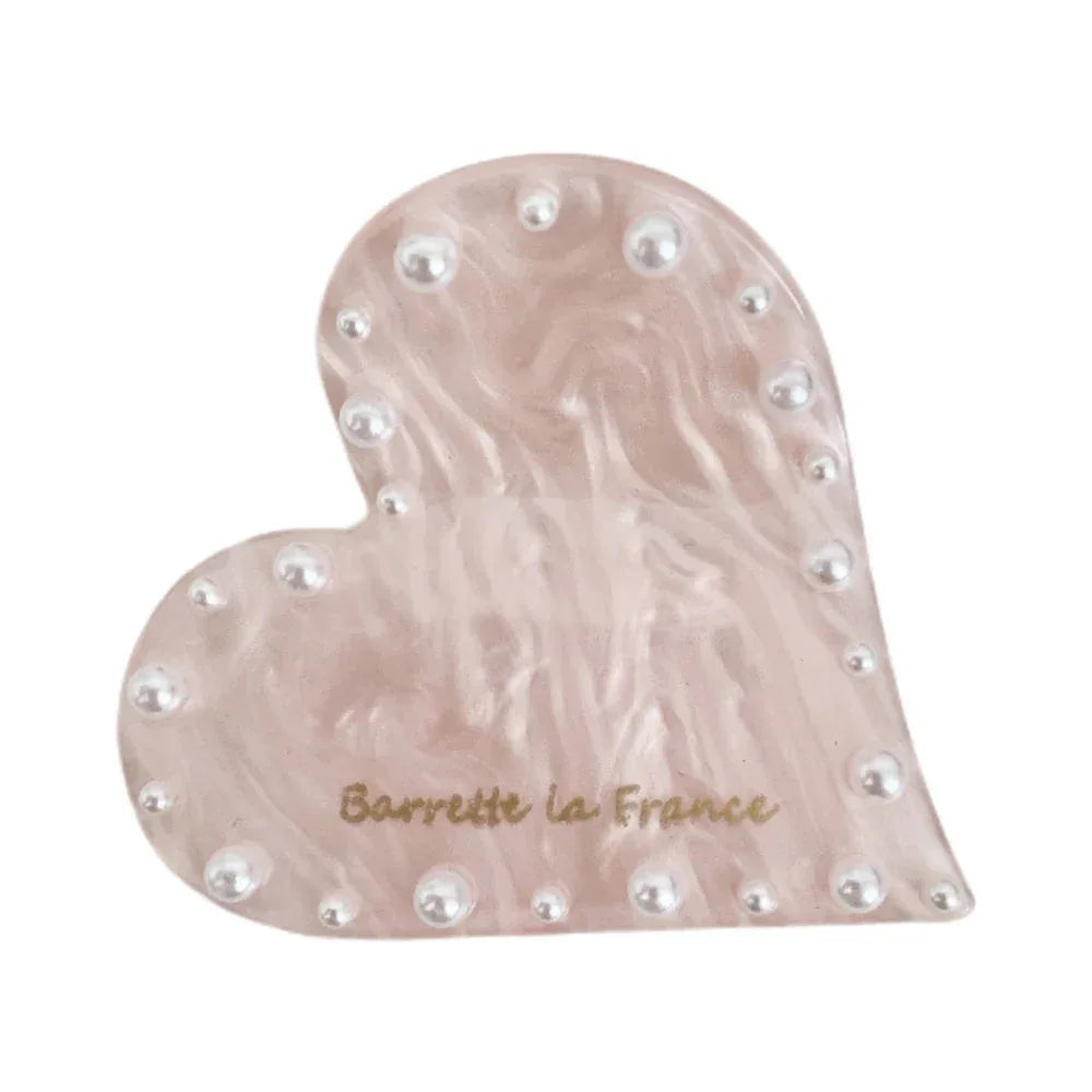 A pink marbled heart-shaped hair clip with faux pearl embellishments and the brand name "Barrette la France" printed in gold.