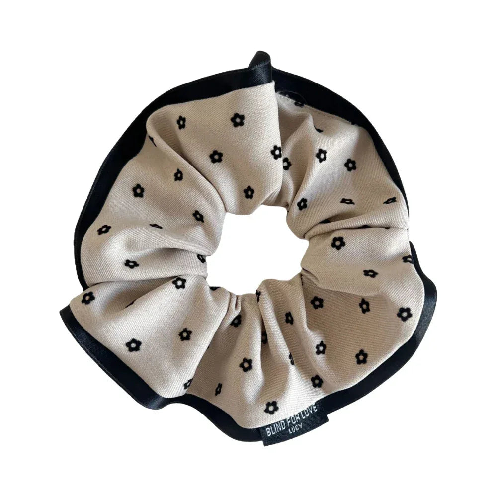 A single scrunchie with a beige background and black floral print, featuring a black satin trim.