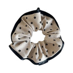 A single scrunchie with a beige background and black floral print, featuring a black satin trim.