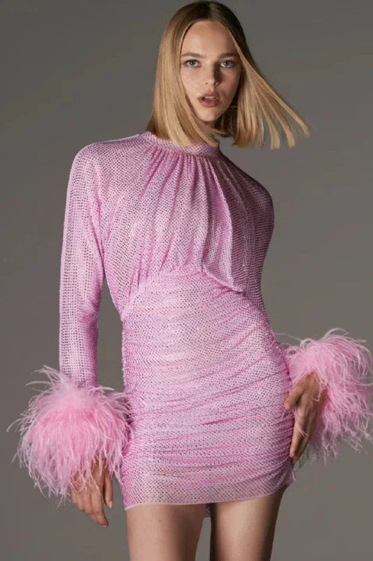 Model wearing a pink long-sleeved mini dress with feather cuffs and sparkling embellishments.