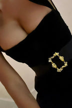 Model posing in a black velvet mini dress with a square neckline and gold buckle belt