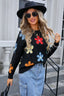 Woman wearing a black long-sleeve sweater with a colorful floral print, denim skirt, black hat, and sunglasses.