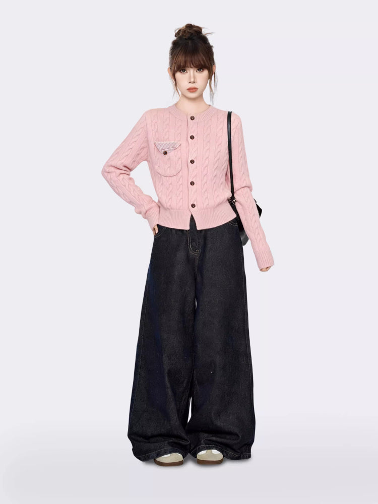 Full body shot of a woman in a pink cable knit cardigan and dark wide-leg jeans, posing with hands in pockets.