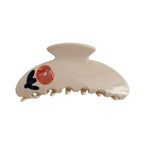 A cream-colored claw clip with a red floral design and a small gemstone.