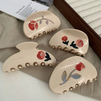 A collection of cream-colored claw clips with red floral designs.