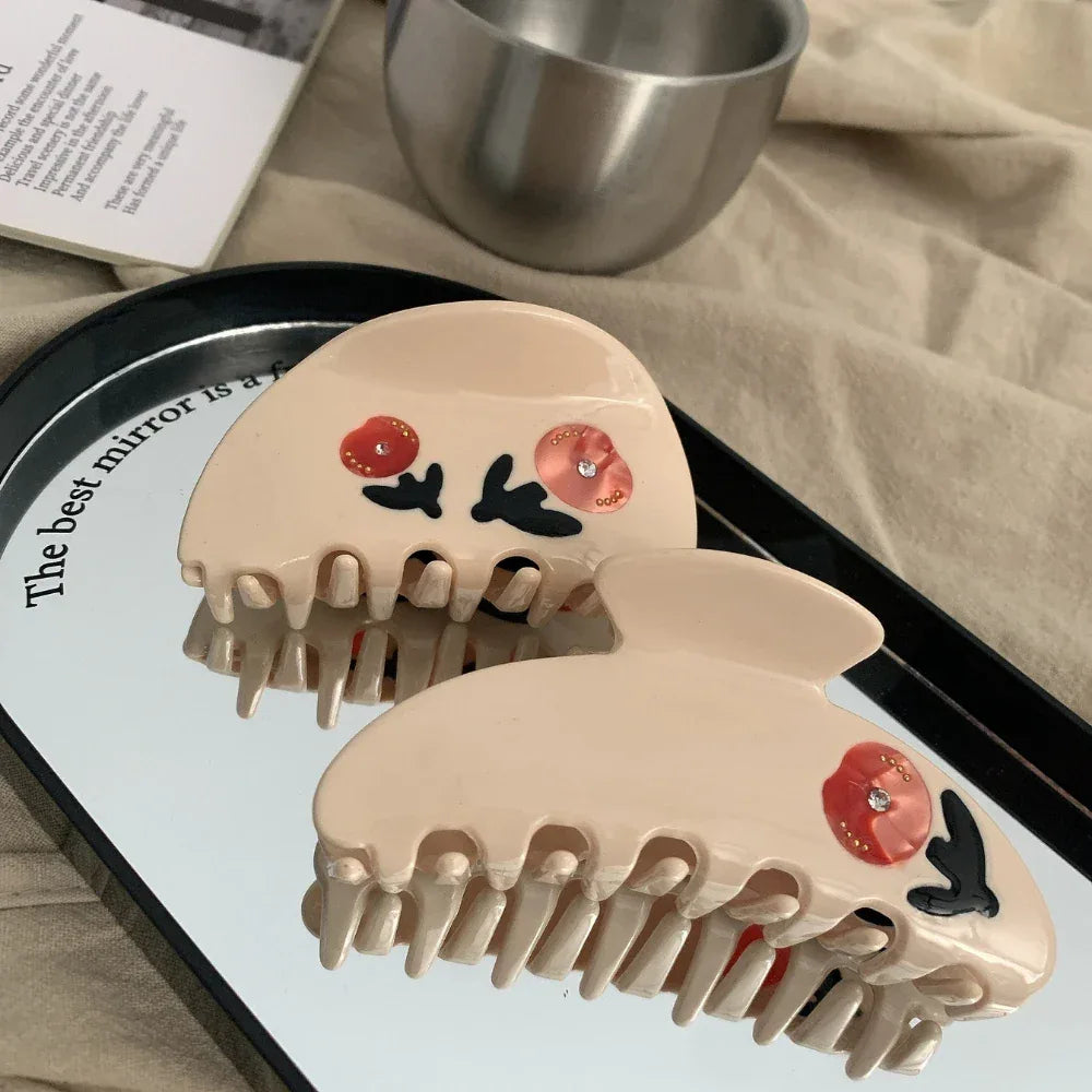Two cream-colored claw clips with red floral designs reflected on a mirrored surface.