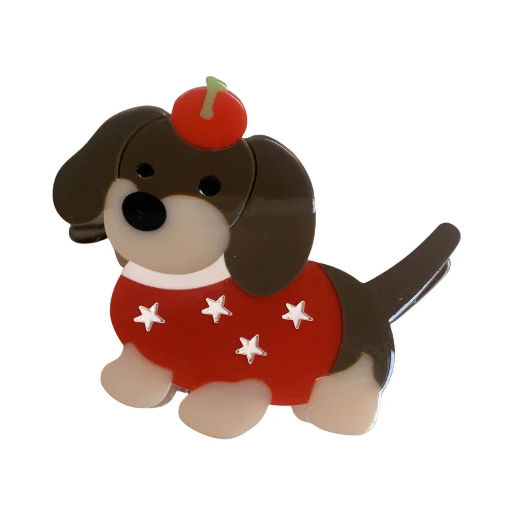 A cute acrylic dachshund dog brooch with a red sweater adorned with white stars and a red apple on its head.