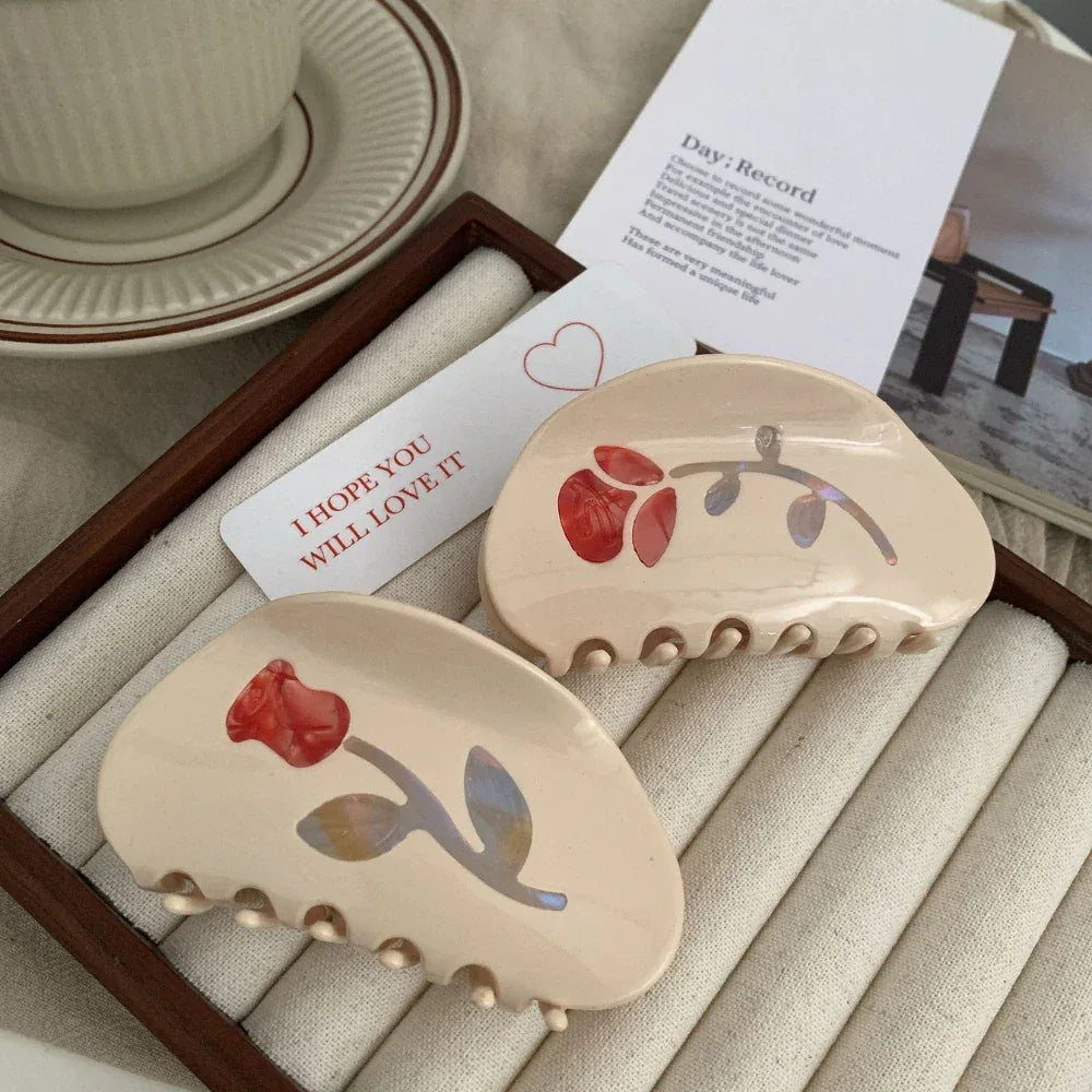 Two cream-colored claw clips with red floral designs displayed next to a card.