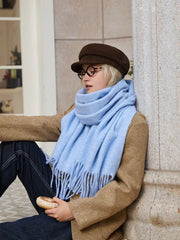 A young woman sits by a pillar, wearing a light blue fringed scarf and a brown tweed jacket, holding a pastry.