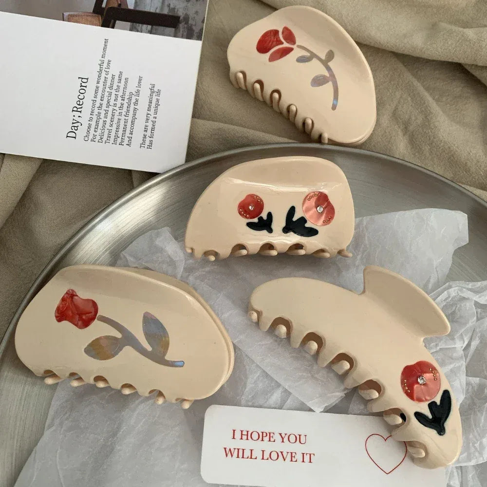 Four cream-colored claw clips with red floral designs arranged on a surface.