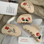 Four cream-colored claw clips with red floral designs arranged on a surface.