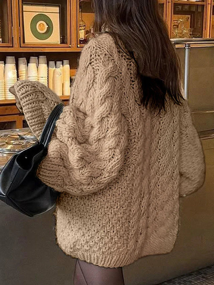 back view of a woman wearing a beige chunky cable knit oversized sweater with a black handbag
