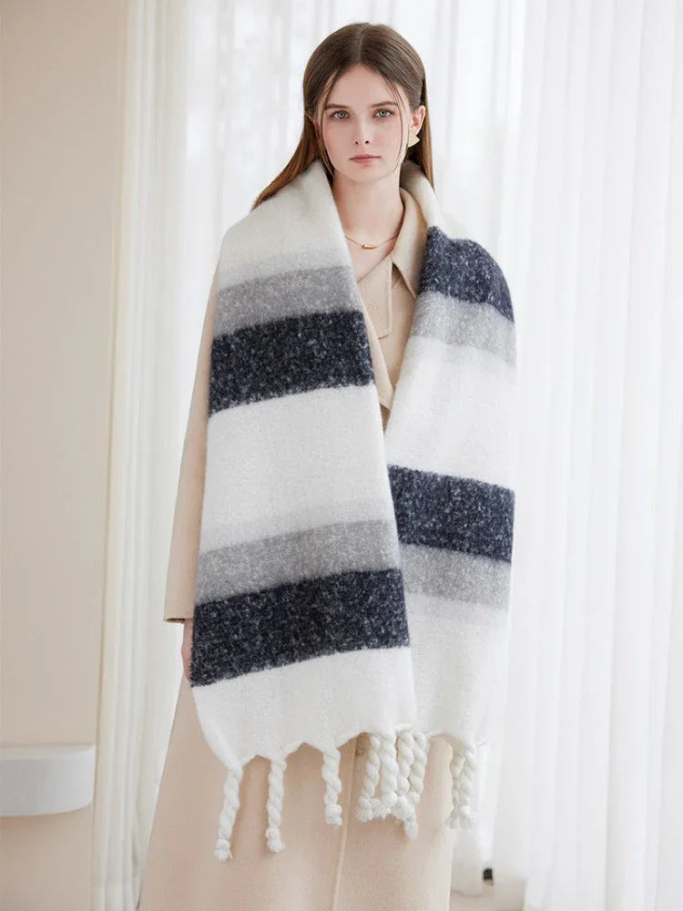 Woman wearing a cream coat and a large, striped scarf with white, grey, and dark blue bands and white fringe details.