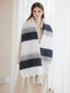 Woman wearing a cream coat and a large, striped scarf with white, grey, and dark blue bands and white fringe details.