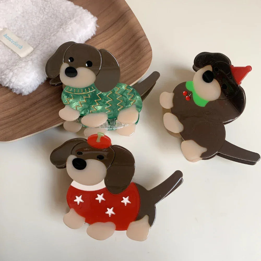 A top-down view of three charming acrylic dachshund dog brooches. They are arranged on a white surface, showcasing their individual festive designs.