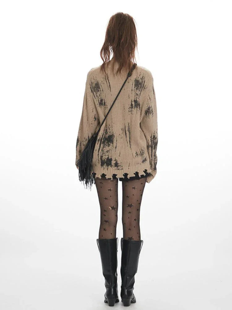 Back view of a model wearing a distressed knit cardigan with a graphic print, paired with black shorts, star-patterned tights, and black boots.