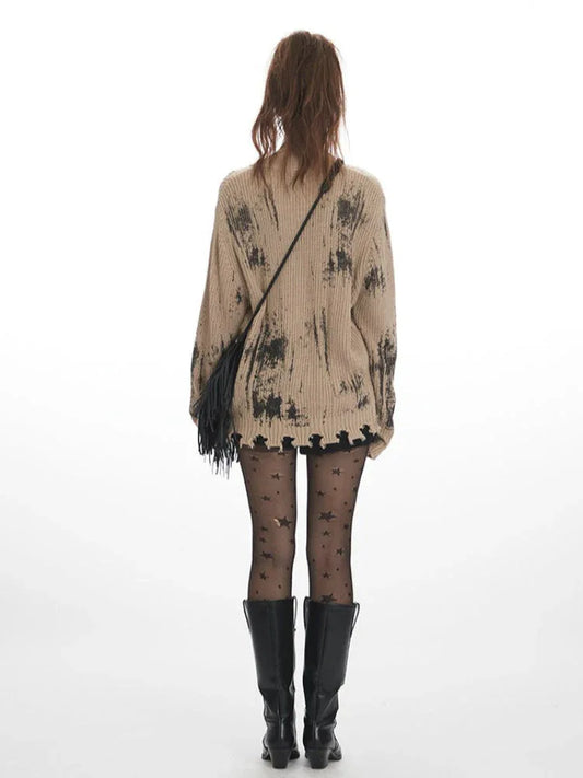 Back view of a model wearing a distressed knit cardigan with a graphic print, paired with black shorts, star-patterned tights, and black boots.