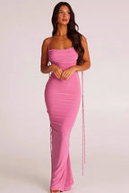 Woman wearing a long pink ruched dress with spaghetti straps and an open back