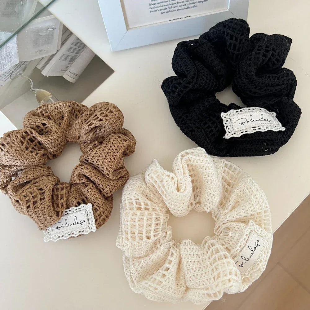 Three crocheted scrunchies in black, brown, and white laid out on a white surface