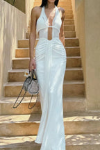 Woman in a white halter neck maxi dress with a plunging neckline and ruched detailing, standing on stairs.