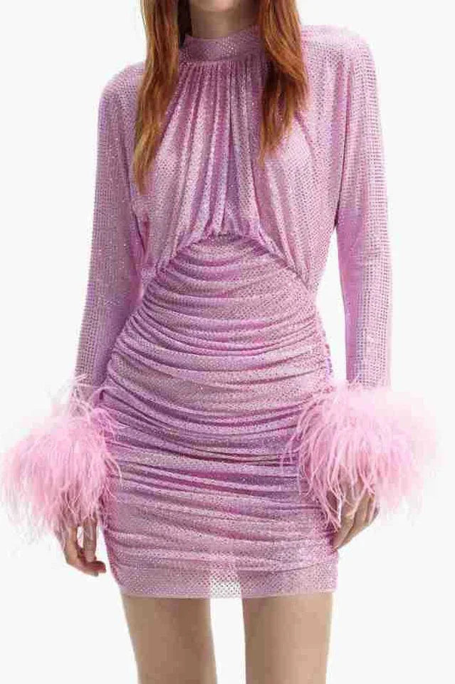 Full-body shot of a woman in a pink ruched mini dress with feather cuffs.