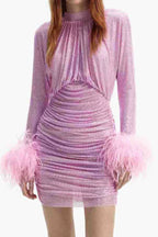 Full-body shot of a woman in a pink ruched mini dress with feather cuffs.