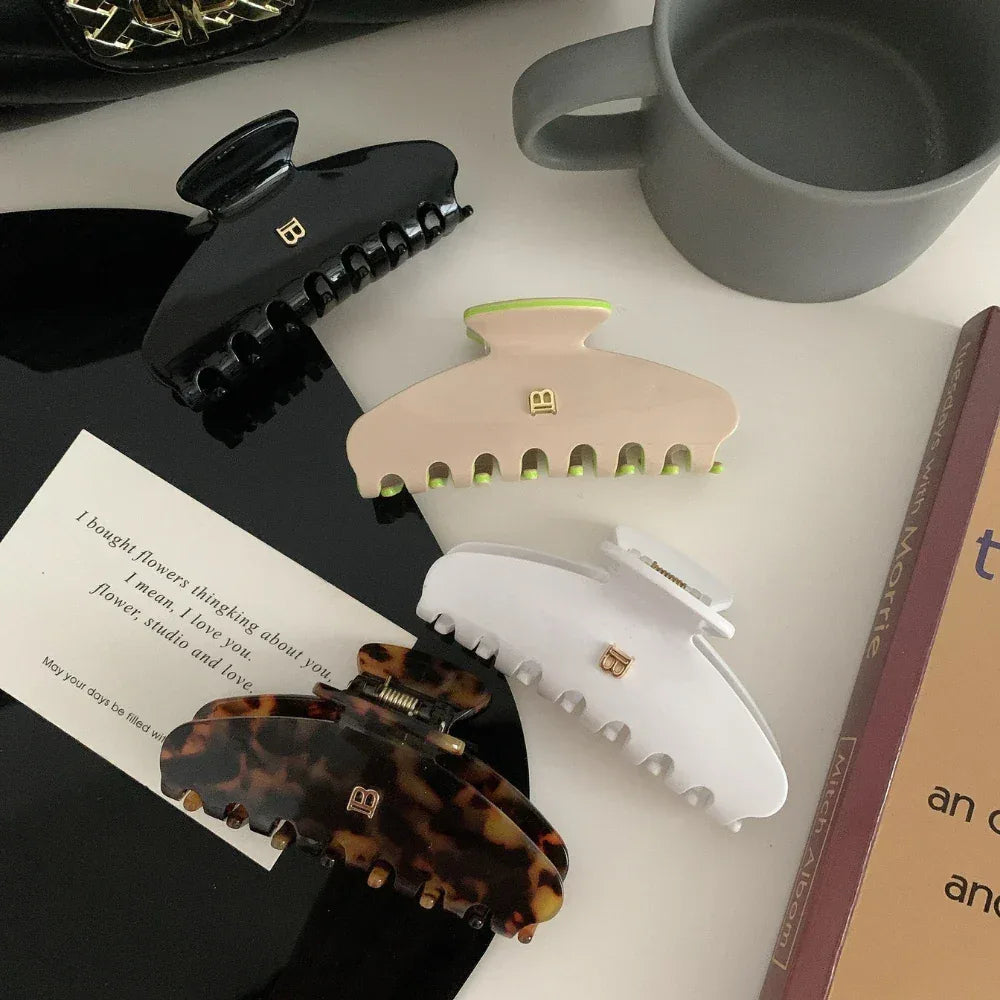 Four hair claw clips arranged on a surface: black, white, beige with neon green accents, and tortoise shell