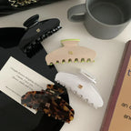 Four hair claw clips arranged on a surface: black, white, beige with neon green accents, and tortoise shell
